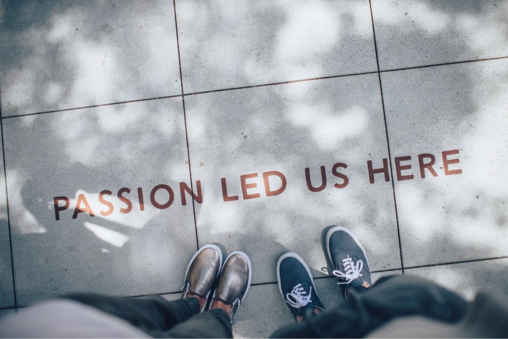 Two men standing over a sidewalk that has writing 'passion led us here'